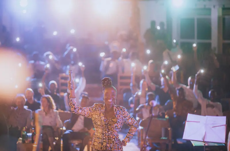 Une chanteuse sourit, micro levé, devant le public qui brandit ses téléphones